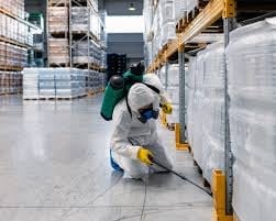 Worker in safety gear inspecting inventory in an industrial warehouse with metal shelving and storage containers